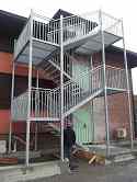 Emergency stairs from galvanized steel. Staircase balustrade with stainless steel high polished, tubular handrail and filling from galvanized steel bars. Mesh steel flooring used for landings and steps